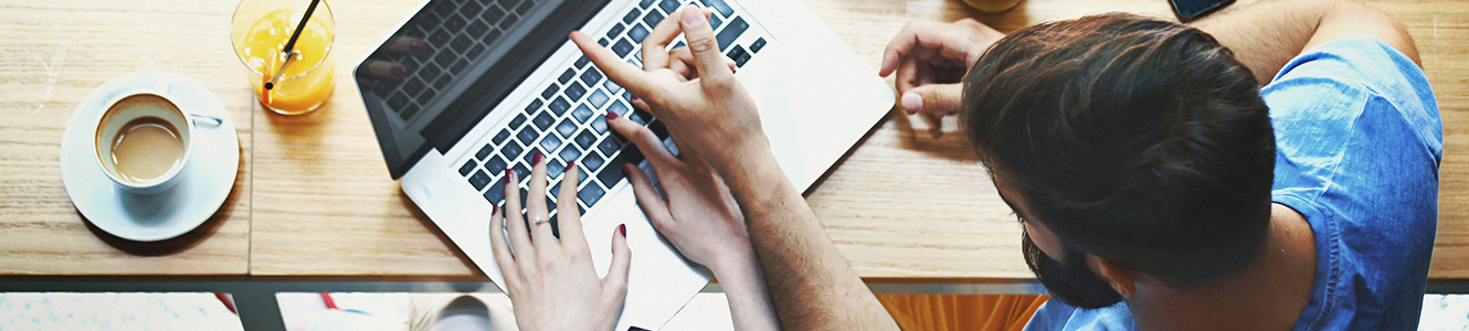 Man and woman sitting at coffee shop table working on a laptop together.